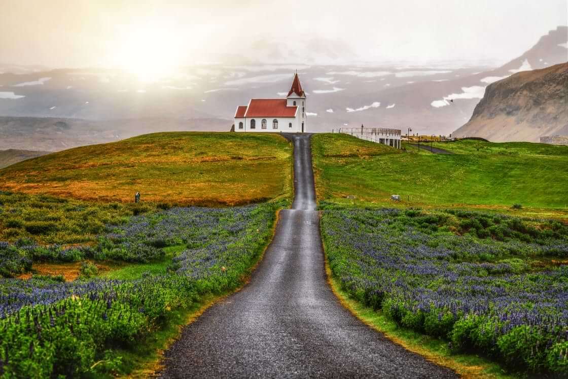 A long road leads to a lone white church in Hellissandur, Iceland. © Blue Planet Studio/stock.adobe.com