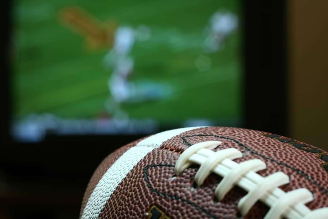 A football sits in front of a TV. The He Gets Us campaign plans to spend nearly $20 million for sixty second of airtime during Super Bowl LVII this Sunday. © By JJAVA/stock.adobe.com