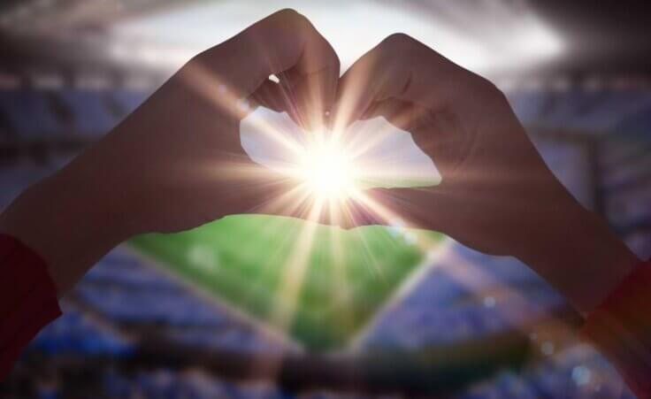 A woman forms her hands to make a heart shape with a football stadium in the background. © By WavebreakMediaMicro/stock.adobe.com. Both Valentine's Day and the Super Bowl can remind us of God's love.