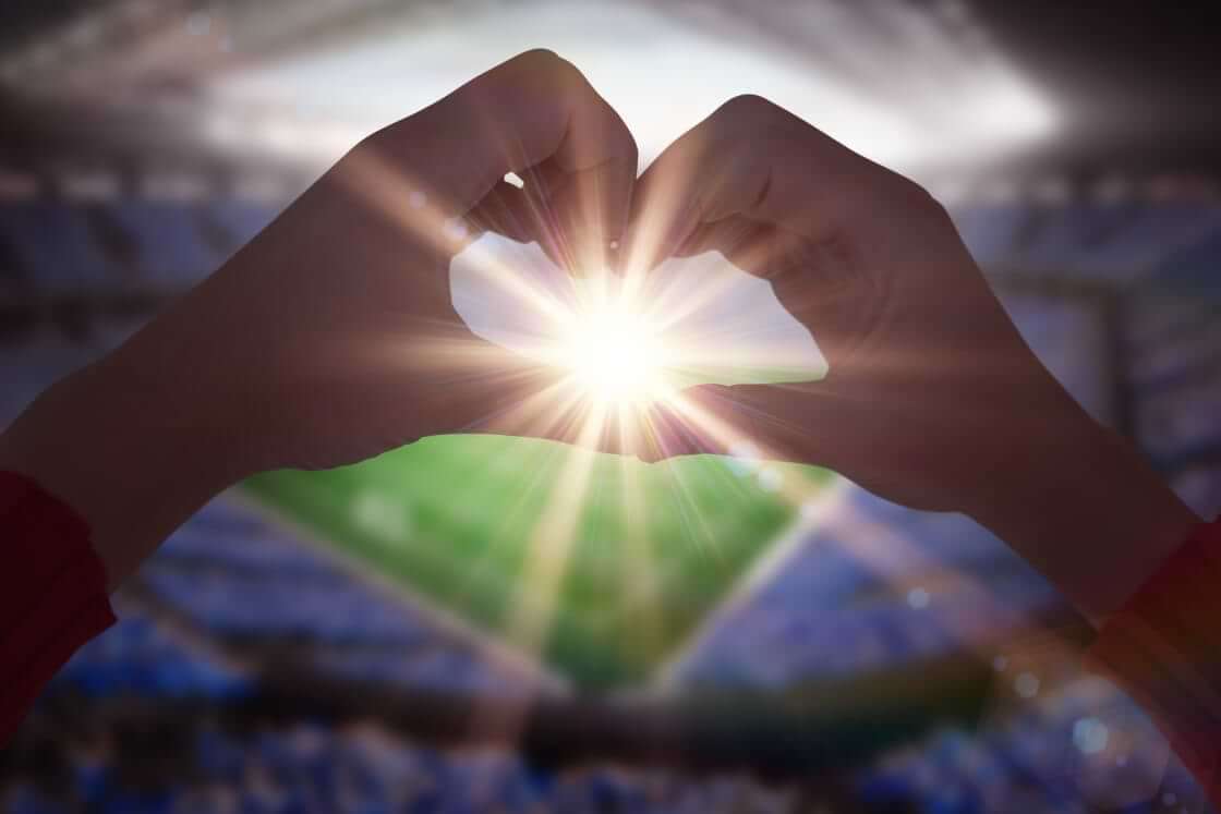 A woman forms her hands to make a heart shape with a football stadium in the background. © By WavebreakMediaMicro/stock.adobe.com. Both Valentine's Day and the Super Bowl can remind us of God's love.
