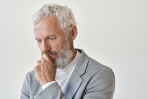 A thoughtful older man with gray hair in a gray sport coat rests his left hand on his chin while looking down in a pensive mood. © By insta_photos/stock.adobe.com