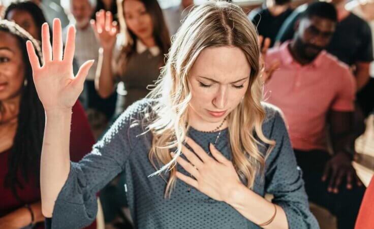 STOCK PHOTO: A woman holds her right and in the air and places her left hand over her heart, signaling a moment of worship. © By rawpixel.com/stock.adobe.com. The 2023 Asbury revival is witnessing similar moments across hundreds of people.