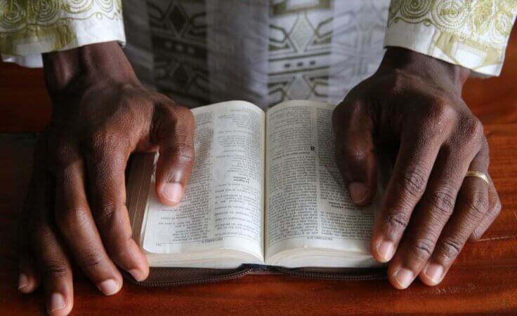 A Christian African man reads an open Bible, his hands resting on either side of God's word. Evangelism in Africa is often motivated by gratitude more than duty, as can be typical of Western Christianity. © By Godong Photo/stock.adobe.com