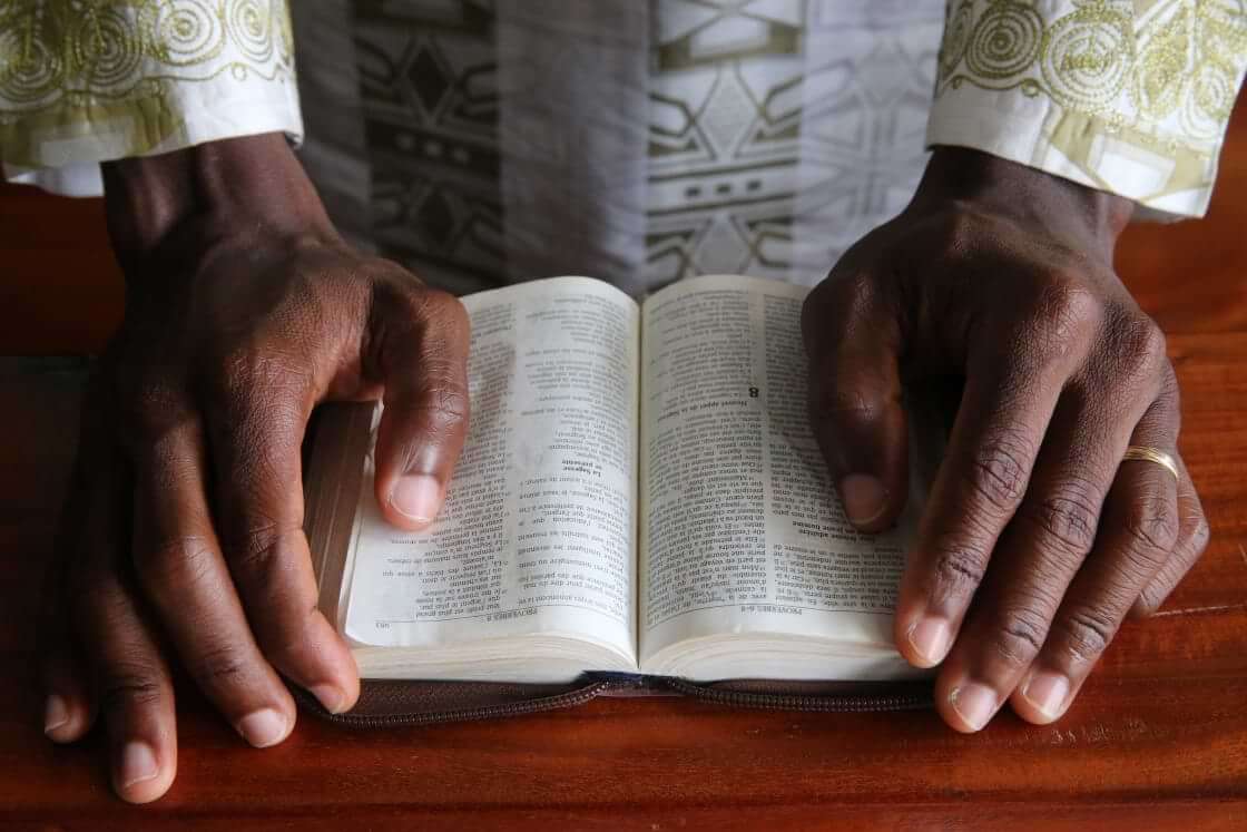 A Christian African man reads an open Bible, his hands resting on either side of God's word. Evangelism in Africa is often motivated by gratitude more than duty, as can be typical of Western Christianity. © By Godong Photo/stock.adobe.com