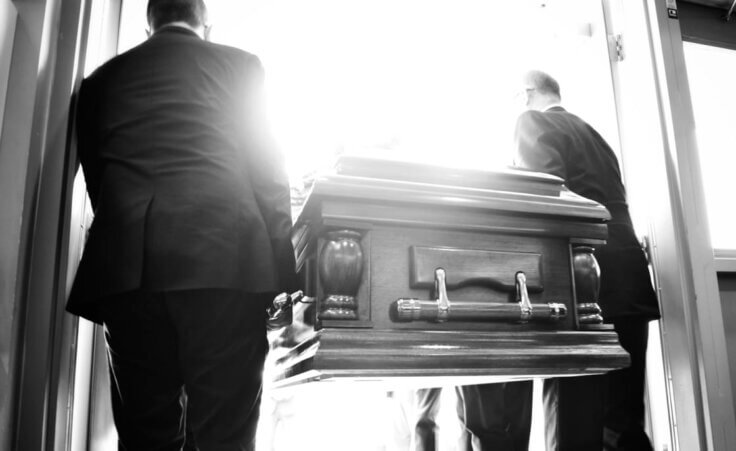 Two men carrying a coffin outside, black and white. Are you living in light of "eulogy virtues?"