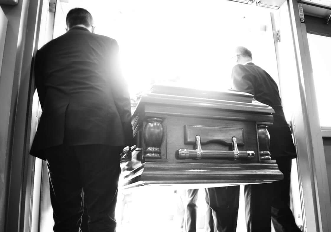 Two men carrying a coffin outside, black and white. Are you living in light of "eulogy virtues?"