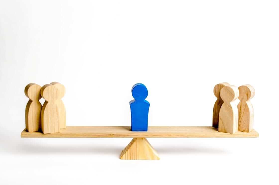 Seven wooden figures are perched on a wooden seesaw, three on the left, three on the right, and one painted blue in the middle symbolizing conflict avoidant pastors and church leaders. © By Andrii Yalanskyi/stock.adobe.com