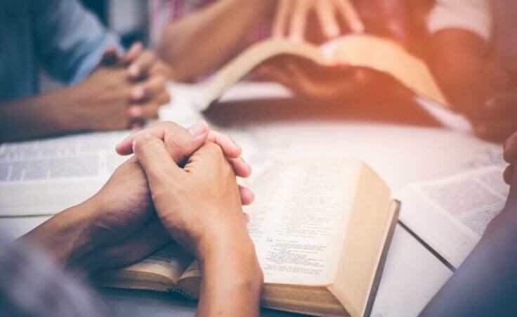 A Bible study group is gathered around a table, Bibles open, hands clasped in prayer, indicative of what the church is © By brain2hands/stock.adobe.com