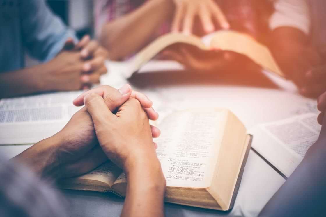A Bible study group is gathered around a table, Bibles open, hands clasped in prayer, indicative of what the church is © By brain2hands/stock.adobe.com