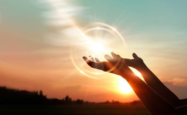 A woman prays with her hand turned upwards against a sunset. A circular sunburst appears around her hands, reminiscent of the pearl of great price Jesus speaks about in Matthew 13. © By ipopba/stock.adobe.com