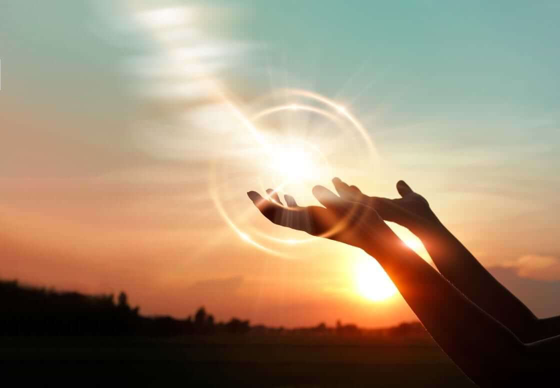 A woman prays with her hand turned upwards against a sunset. A circular sunburst appears around her hands, reminiscent of the pearl of great price Jesus speaks about in Matthew 13. © By ipopba/stock.adobe.com