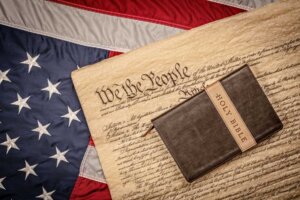 A Bible lays atop the US Constitution, which lays atop an American flag, illustrating the ongoing debates in America over religious freedom. © By cherylvb/stock.adobe.com