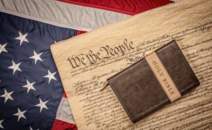 A Bible lays atop the US Constitution, which lays atop an American flag, illustrating the ongoing debates in America over religious freedom. © By cherylvb/stock.adobe.com