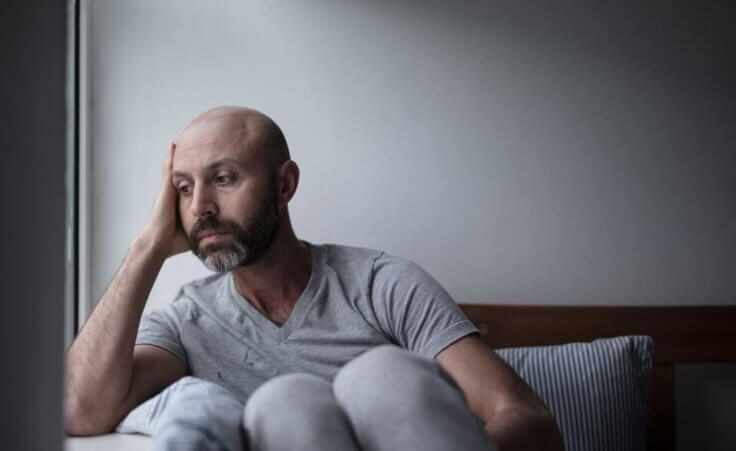 Depressed man looks out the window while in bed.