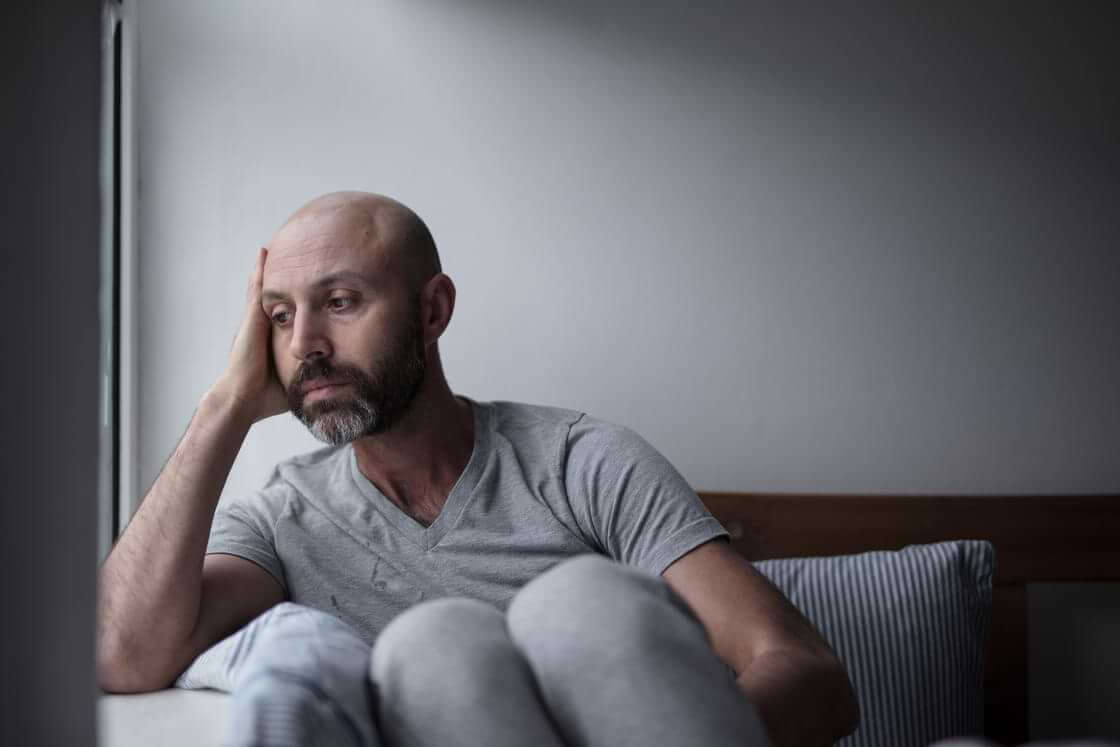Depressed man looks out the window while in bed.