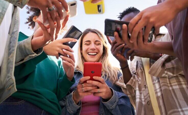 A group of Gen Z young adults stands in a circle, all using smartphones. © By By CarlosBarquero/stock.adobe.com