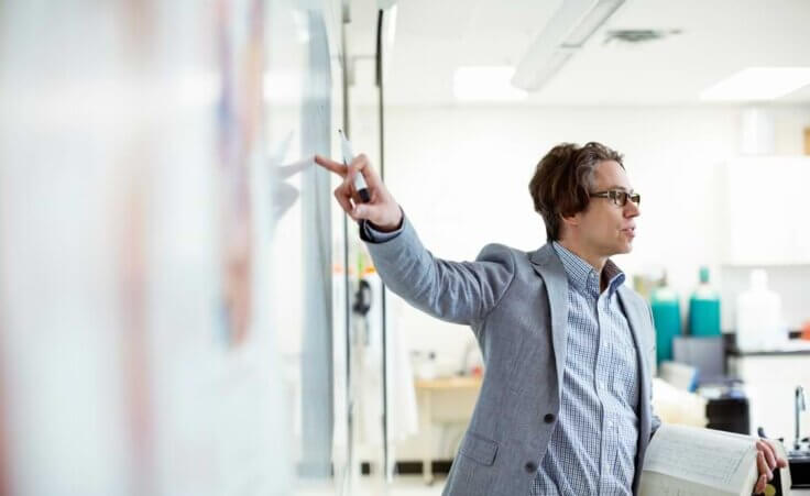 Professor teaching at class, pointing to a white board