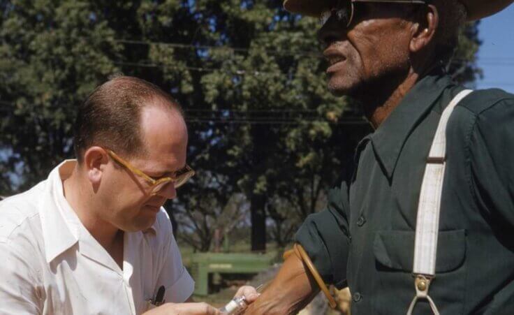 FILE - In this 1950's photo made available by the National Archives, a man included in a syphilis study has blood drawn by a doctor in Alabama. For 40 years starting in 1932, medical workers in the segregated South withheld treatment for Black men who were unaware they had syphilis, so doctors could track the ravages of the illness and dissect their bodies afterward. (National Archives via AP) Health inequality in the US still exists today.
