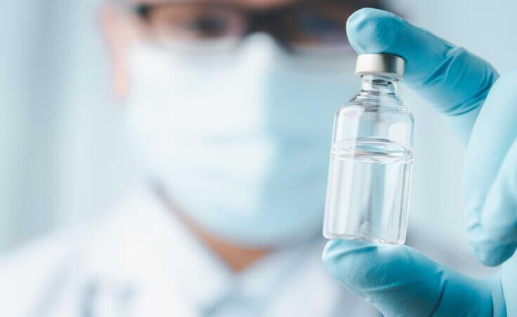 A doctor wearing glasses and a facemask holds a vaccine vial between his fingers in front of him. Moderna's chief medical officer Dr. Paul Burton believes vaccines for cancer and a range of other conditions could be available in five years. © By Looker_Studio/stock.adobe.com