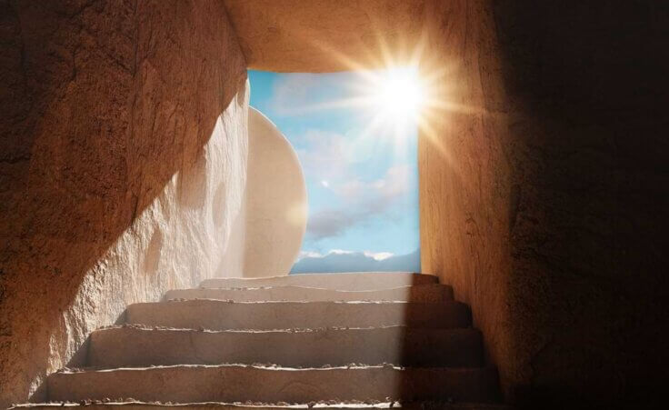 Steps within a dark tomb lead up to an opening where a stone has been rolled away as a bright sun shines through, a scene evoking Easter Sunday morning. © By PhotoGranary/stock.adobe.com