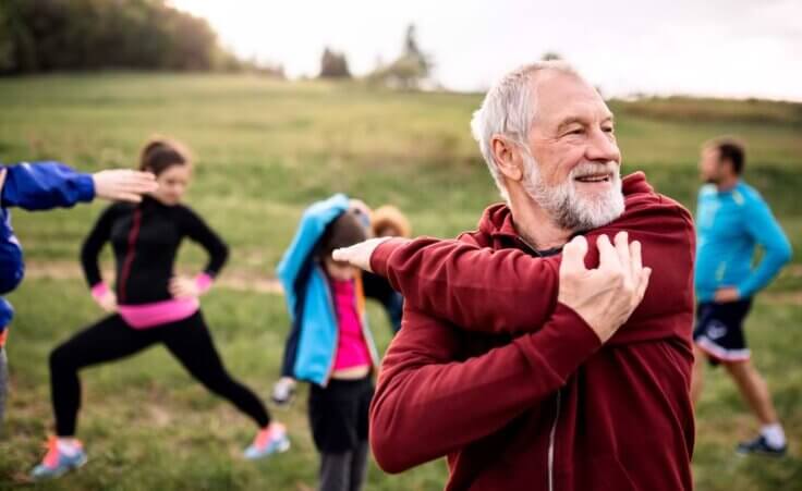 Large group of fit and active people doing exercise in nature, stretching