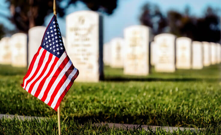 A lone American flag stands in front of multiple gravestones on Memorial Day. © By Bill Chizek/stock.adobe.com