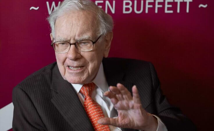 Warren Buffet gesturing and talking at a shareholders meeting.