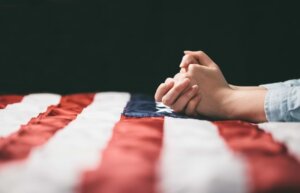 A woman's hands are clasped in prayer on top of an American flag © By 4Max/stock.adobe.com / What should we make of American morality?
