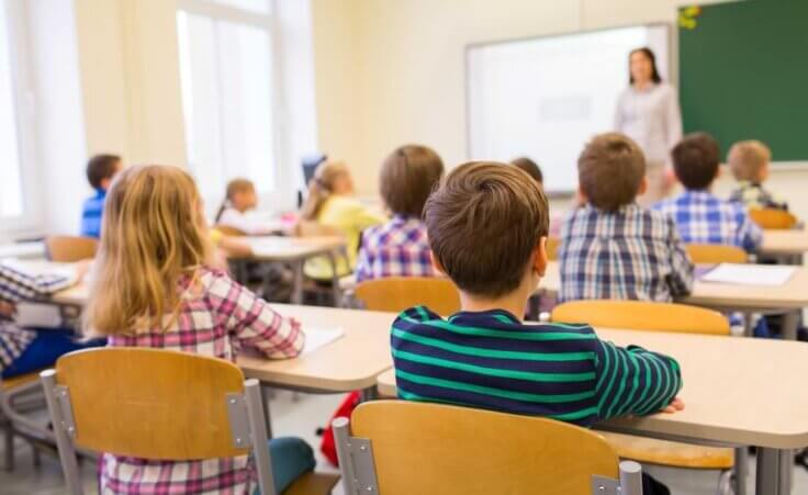 A classroom full of seated children at their desks, seen from behind, their teach standing in front. © By Syda Productions/stock.adobe.com. The Texas Senate recently passed a bill requiring the Ten Commandments to be displayed in public school classrooms.