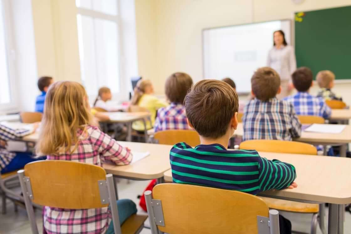 A classroom full of seated children at their desks, seen from behind, their teach standing in front. © By Syda Productions/stock.adobe.com. The Texas Senate recently passed a bill requiring the Ten Commandments to be displayed in public school classrooms.