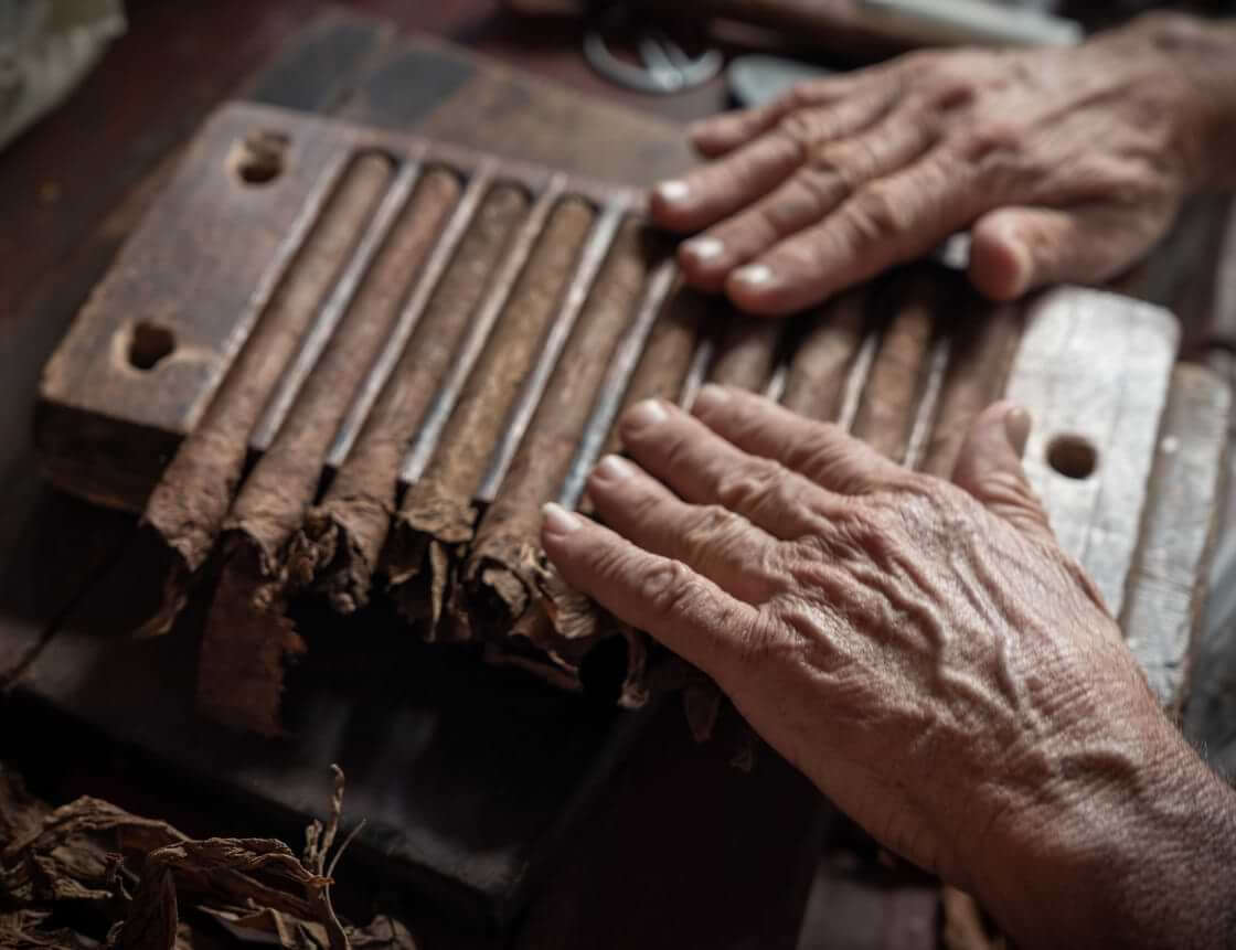 Two hands roll multiple Cuban cigars in a wooden mold created to hold 10 cigars. © By Arsgera/stock.adobe.com