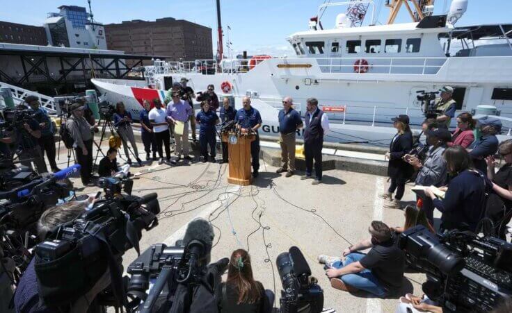 U.S. Coast Guard Capt. Jamie Frederick, center at microphone, faces reporters during a news conference, Wednesday, June 21, 2023, at Coast Guard Base Boston, in Boston. The U.S. Coast Guard says sounds and banging noises have been heard from the search area for Titanic submersible. (AP Photo/Steven Senne)