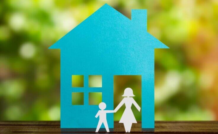 Paper cutouts on top of a table depict a blue home with a single mother holding the hand of her child in front of the home, an illustration of being fatherless. © By paulovilela/stock.adobe.com