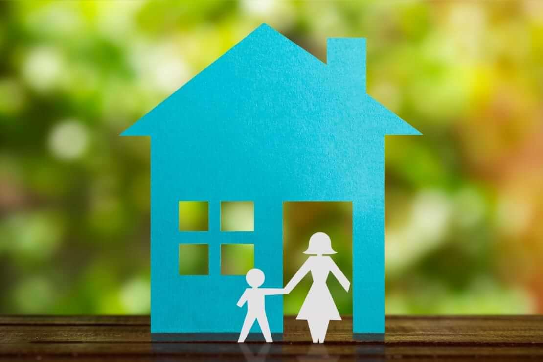 Paper cutouts on top of a table depict a blue home with a single mother holding the hand of her child in front of the home, an illustration of being fatherless. © By paulovilela/stock.adobe.com