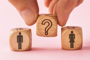 Fingers hold a wooden block emblazoned with a question mark between two other wooden blocks, one depicting a man and one a woman, an illustration of the question: Is cross-dressing a sin? © By Sergey Chayko/stock.adobe.com