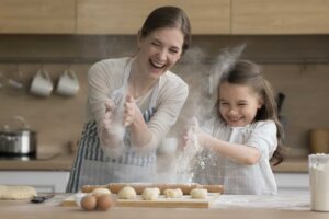 A mother and daughter clap their hands together, sending flour into the air, while making bread. © By fizkes/stock.adobe.com