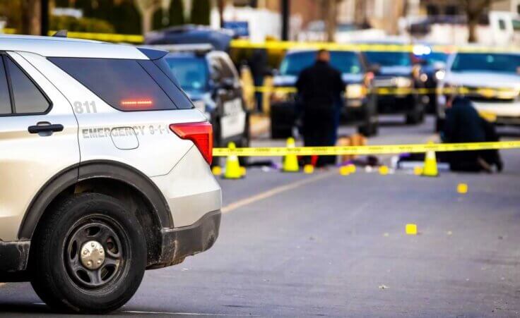 STOCK photo: With a squad car in the foreground, police tape sections off a crime scene as officers investigate. Over the July 4 weekend, 16 mass shootings occurred across 13 states and Washington, D.C. © By PhotoSpirit/stock.adobe.com