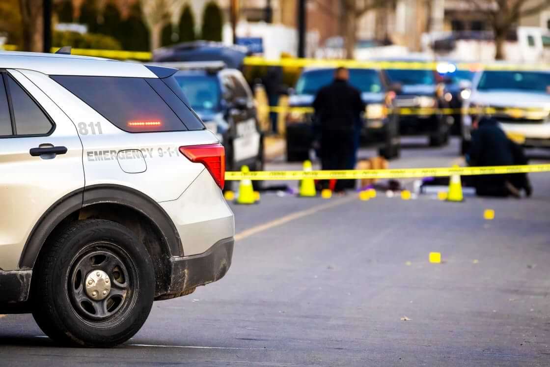 STOCK photo: With a squad car in the foreground, police tape sections off a crime scene as officers investigate. Over the July 4 weekend, 16 mass shootings occurred across 13 states and Washington, D.C. © By PhotoSpirit/stock.adobe.com