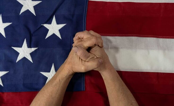 Hands folded in prayer on top of an American flag. © By jn14productions/stock.adobe.com