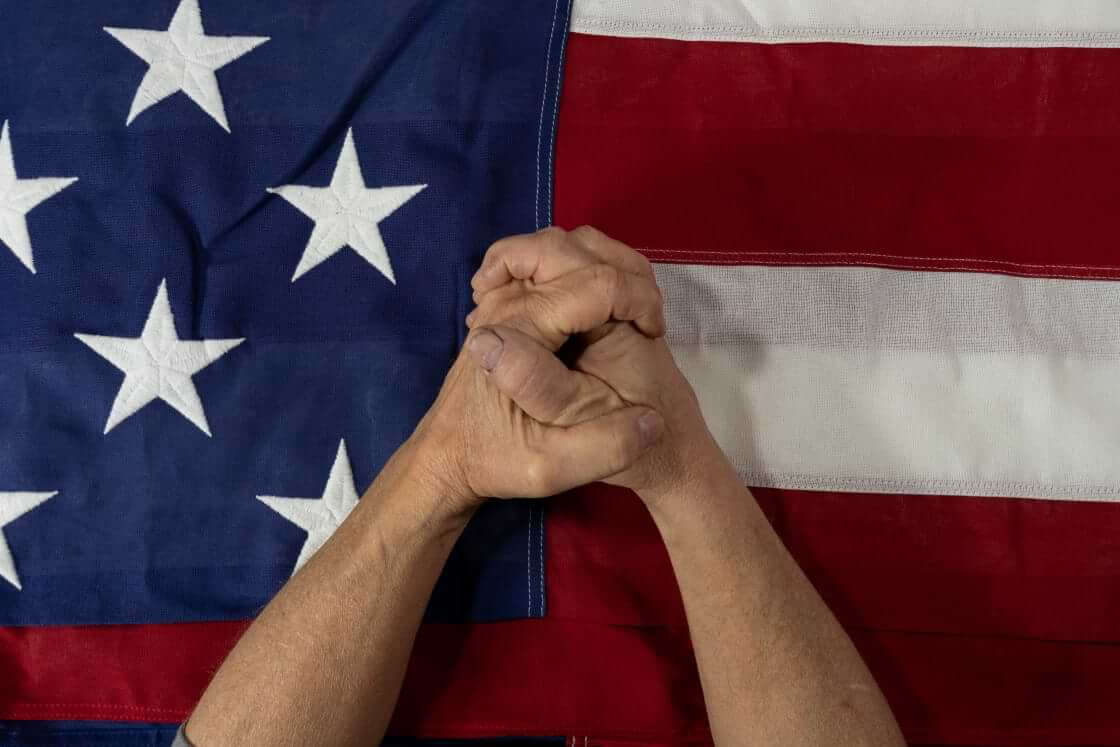 Hands folded in prayer on top of an American flag. © By jn14productions/stock.adobe.com