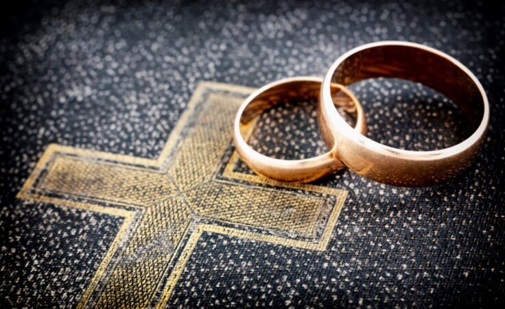 Two wedding rings sit atop an illustration of the cross. © By gaborphotos/stock.adobe.com