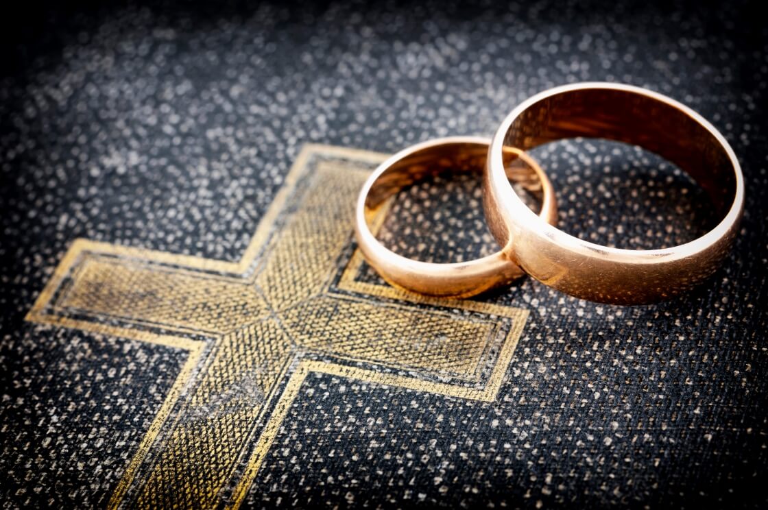Two wedding rings sit atop an illustration of the cross. © By gaborphotos/stock.adobe.com