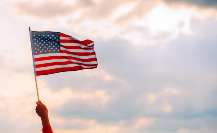 A lone hand waves an American flag in front of a clouds at sunset. © By nicoletaionescu/stock.adobe.com. What role does morality play in a democracy?
