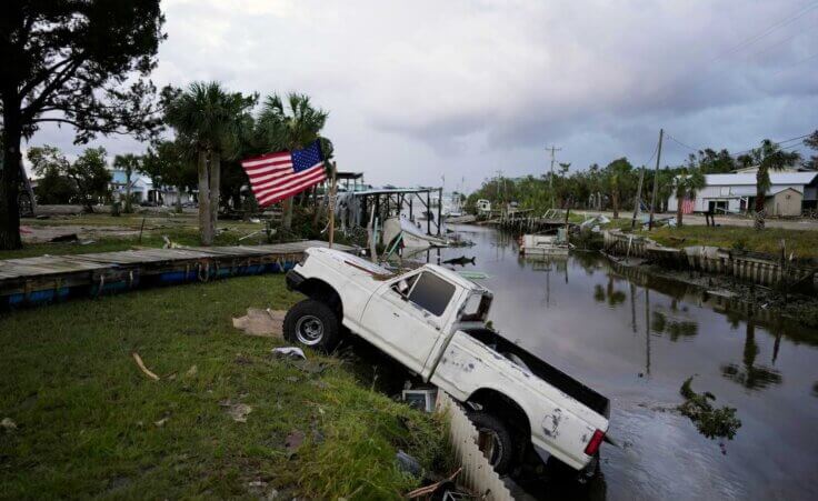 A pickup truck with an American flag tied to sits halfway into a canal in Horseshoe Beach, Fla., after the passage of Hurricane Idalia, Wednesday, Aug. 30, 2023. (AP Photo/Rebecca Blackwell)