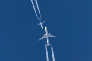 Against a clear blue sky, two white commercial planes appear headed toward each other, an illustration of the increasing number of airline close calls reported over the last month. © By berkut_34/stock.adobe.com