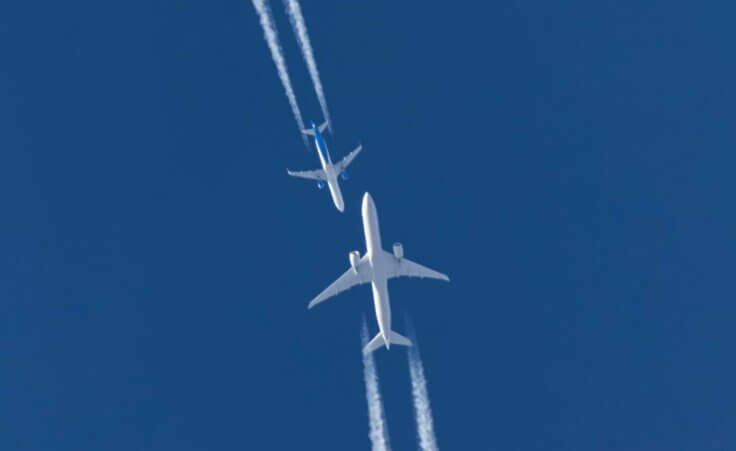 Against a clear blue sky, two white commercial planes appear headed toward each other, an illustration of the increasing number of airline close calls reported over the last month. © By berkut_34/stock.adobe.com