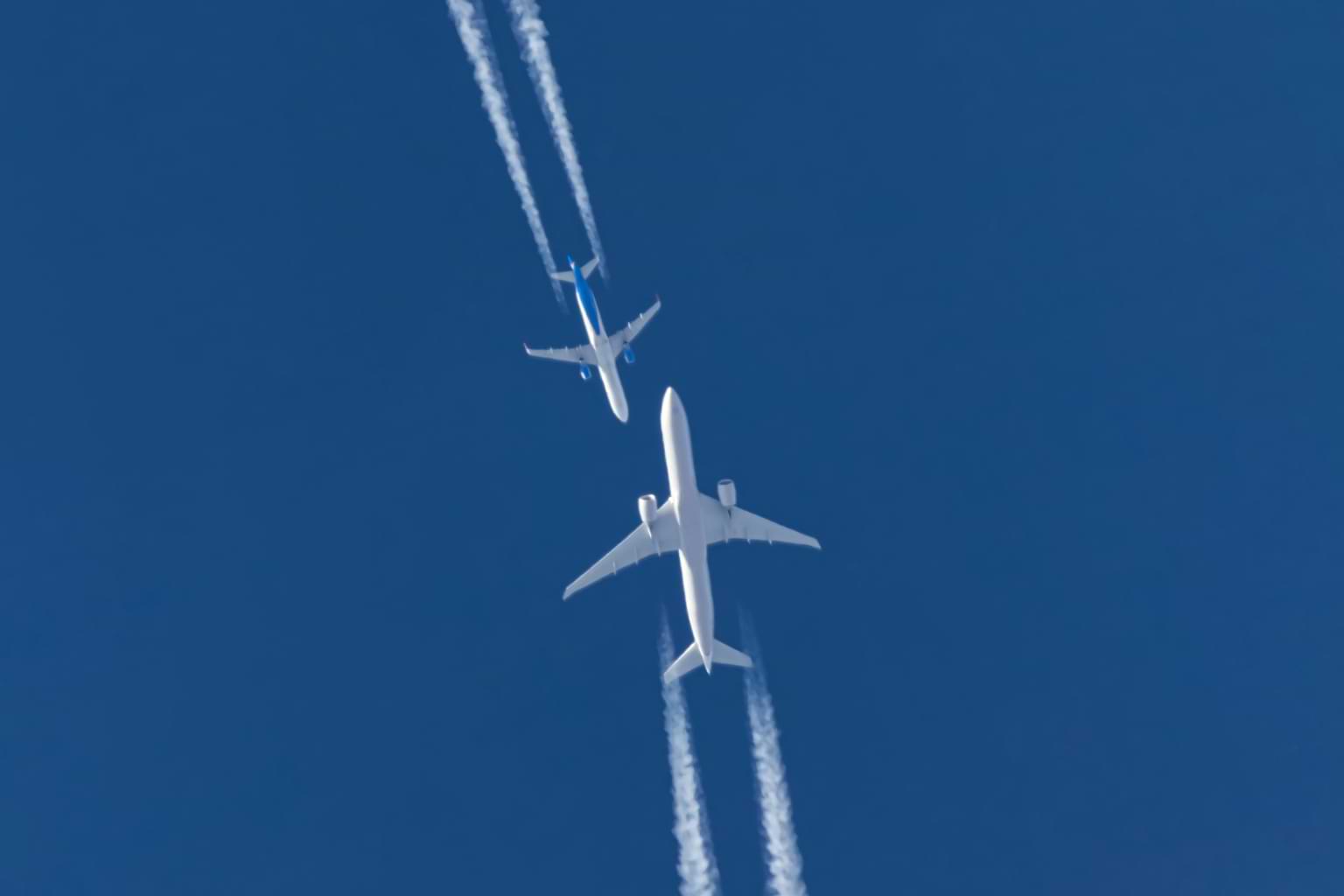 Against a clear blue sky, two white commercial planes appear headed toward each other, an illustration of the increasing number of airline close calls reported over the last month. © By berkut_34/stock.adobe.com