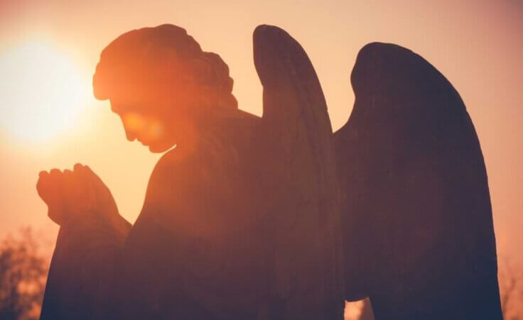 A statue of an angel with its hands folded in prayer in front of a setting sun. © By UMB-O/stock.adobe.com. More Americans believe in angels than they do in hell or the devil.