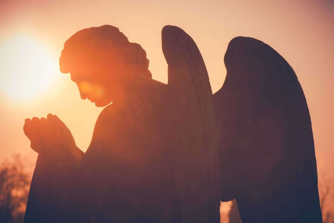 A statue of an angel with its hands folded in prayer in front of a setting sun. © By UMB-O/stock.adobe.com. More Americans believe in angels than they do in hell or the devil.