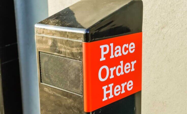A black drive-through speaker with the words "Place Order Here" on the side in a white font on a red background. © By Stephen/stock.adobe.com. AI chatbots could soon be taking over drive-through orders at fast food restaurants across the US.